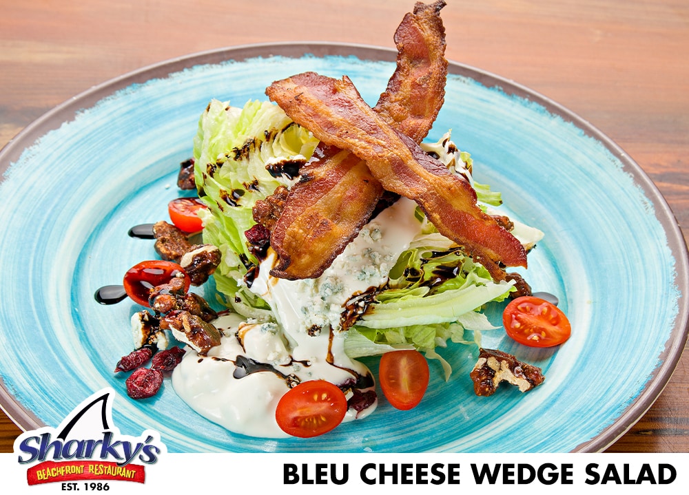 Bleu Cheese Wedge Salad mae with ice cold wedge of Iceberg lettuce with Cherry Tomatoes, Candied Walnuts, dried cranberries, bacon & Applewood Smoked Bleu Cheese. Served with Bleu cheese dressing and a balsamic reduction drizzle